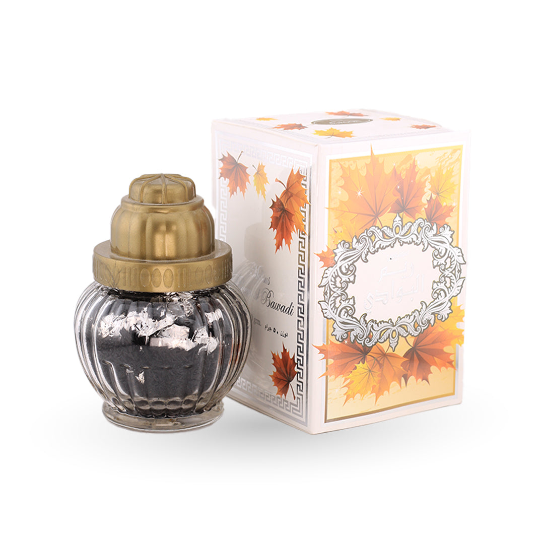 Decorative bottle with gold cap and black interior next to a box with autumn leaf design on a white background